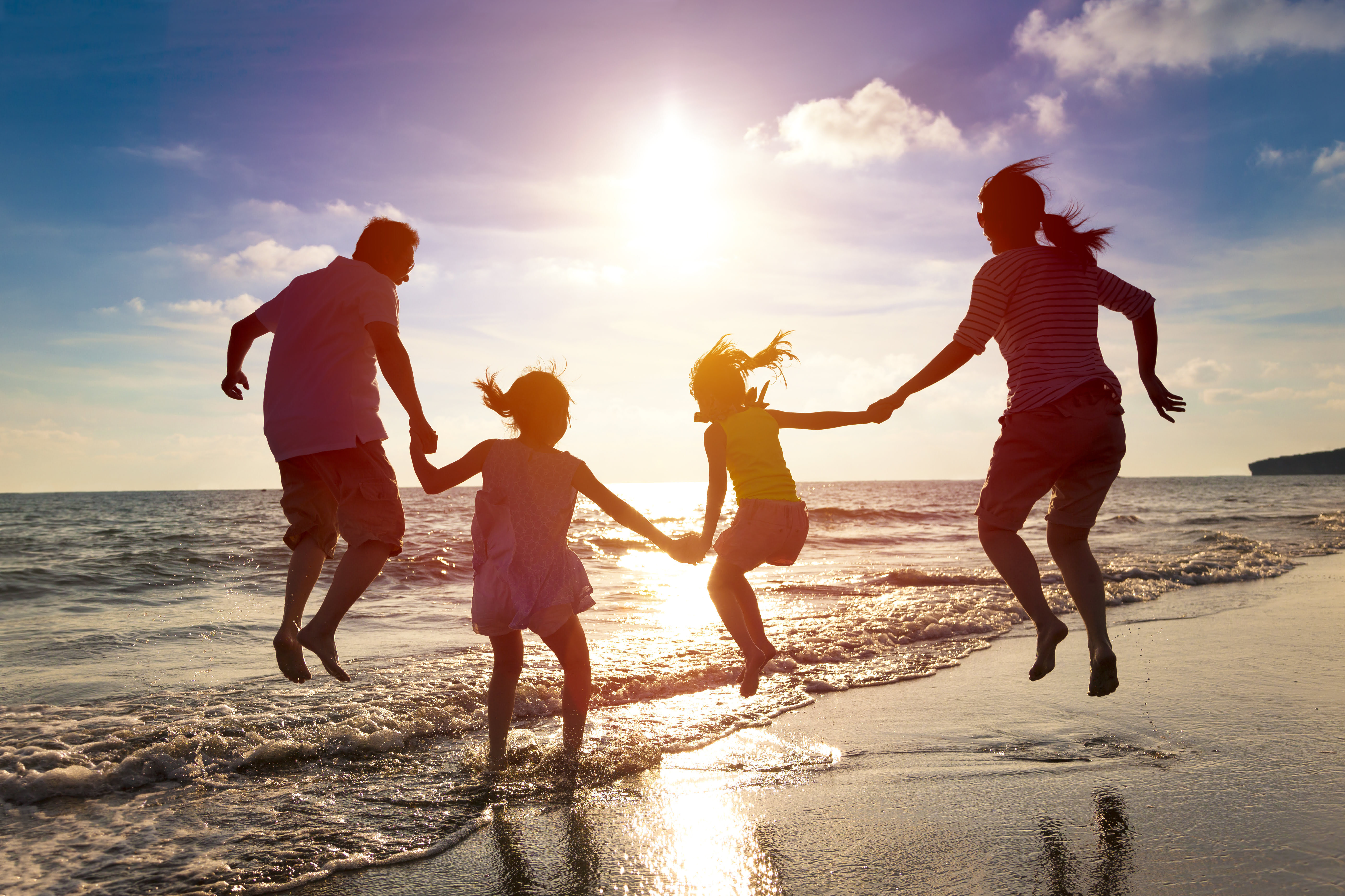 Familie holder i hånd imens de hopper samtidig på stranden ved solnedgangen, fotografi