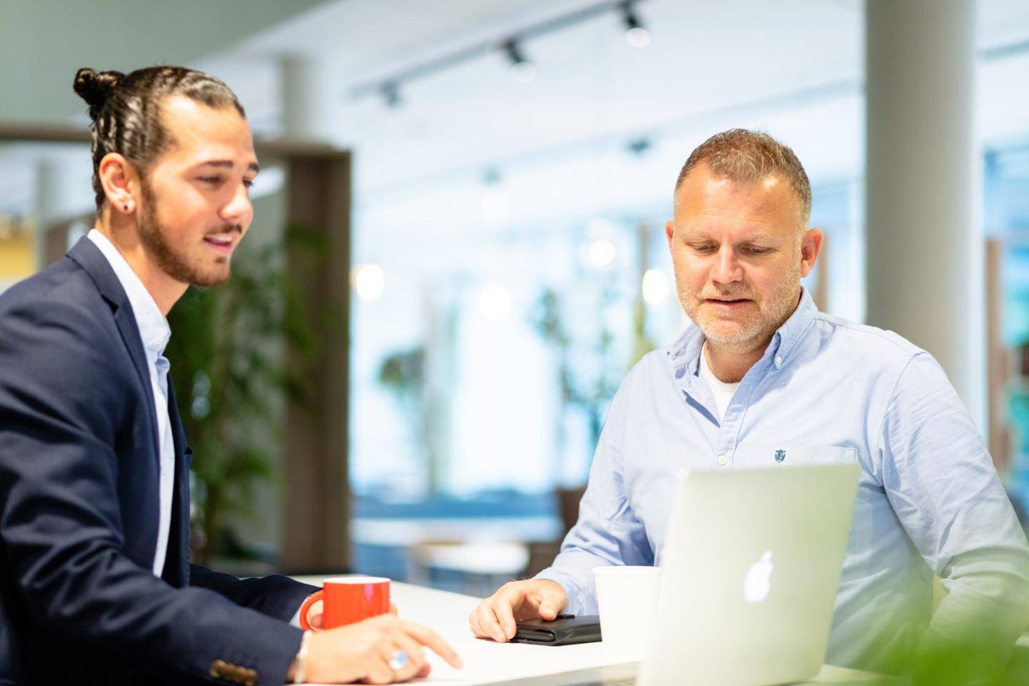 To mænd, der kigger på en computer, hvor den ene har jakkesæt på og den anden en blå skjorte